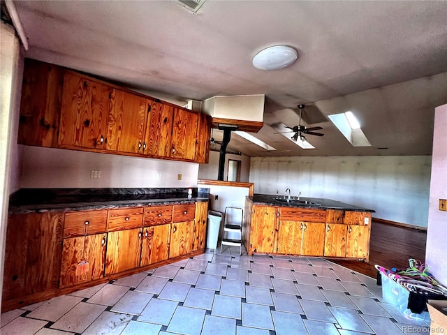 kitchen with ceiling fan, vaulted ceiling with skylight, and sink