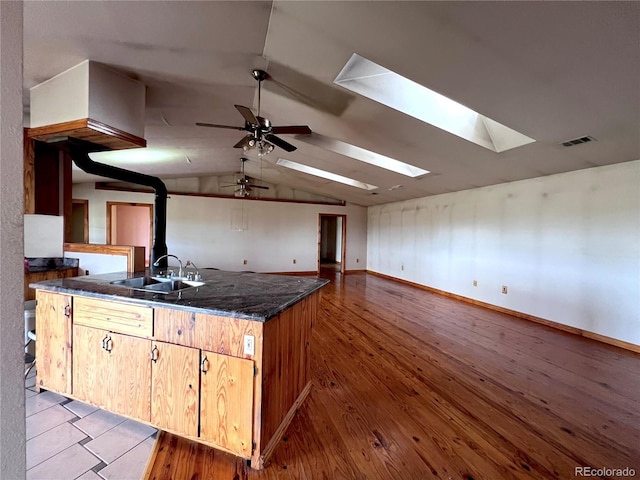 kitchen featuring dark stone countertops, sink, lofted ceiling with skylight, light hardwood / wood-style floors, and ceiling fan