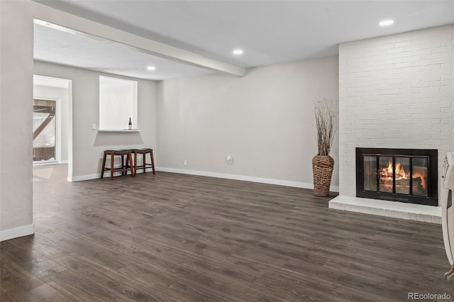 unfurnished living room featuring baseboards, dark wood finished floors, a brick fireplace, beam ceiling, and recessed lighting