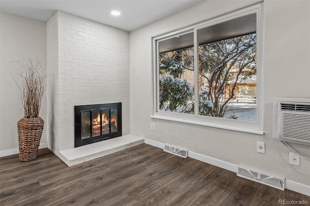 unfurnished living room with a brick fireplace, dark hardwood / wood-style flooring, and an AC wall unit