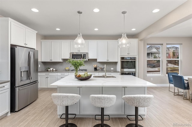 kitchen featuring light wood finished floors, decorative backsplash, stainless steel appliances, and a sink