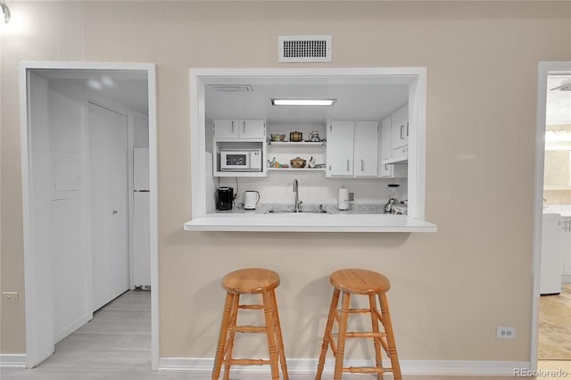 bar with white cabinets, white appliances, sink, and light hardwood / wood-style flooring