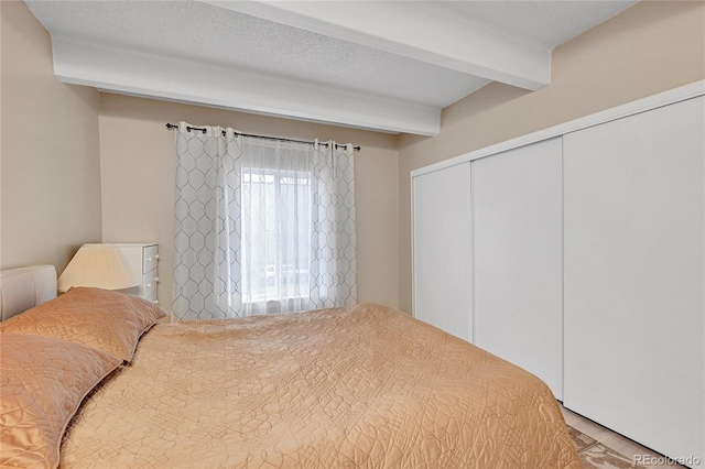 bedroom featuring hardwood / wood-style flooring, beam ceiling, a textured ceiling, and a closet