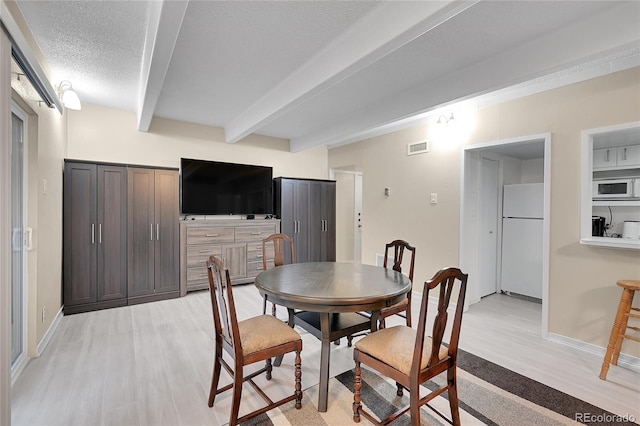 dining room with beam ceiling, a textured ceiling, and light hardwood / wood-style flooring