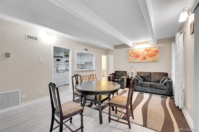 dining room with beamed ceiling, a textured ceiling, light hardwood / wood-style flooring, and sink