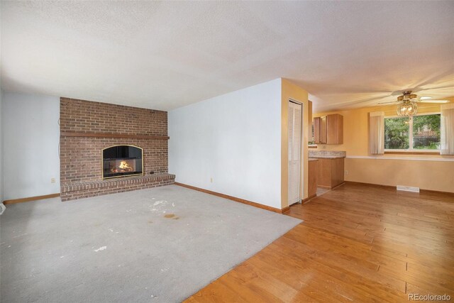 8269 Zephyr St, Arvada, CO 80005 - unfurnished living room with a brick fireplace, a textured ceiling, baseboards, a ceiling fan, and light wood-style floors