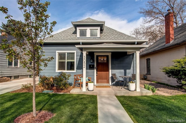 bungalow-style home featuring covered porch, a shingled roof, and a front yard