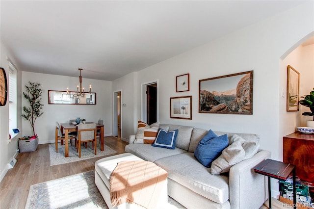 living area featuring arched walkways, baseboards, a chandelier, and light wood-style floors