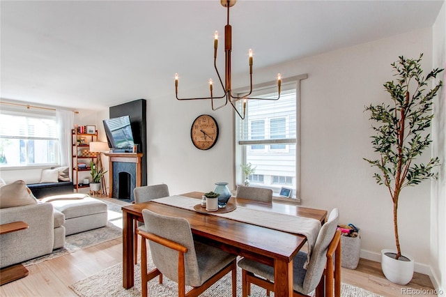 dining area featuring a fireplace with raised hearth, a chandelier, and light wood-style floors