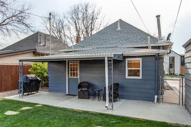 rear view of house with fence, roof with shingles, a chimney, a gate, and a patio area