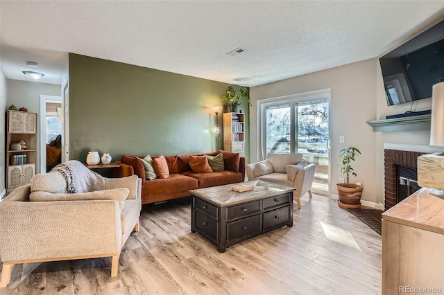 living room with a textured ceiling, a brick fireplace, and light wood-type flooring