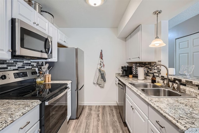 kitchen featuring sink, appliances with stainless steel finishes, white cabinetry, hanging light fixtures, and light wood-type flooring