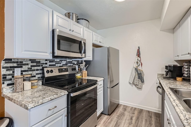 kitchen with tasteful backsplash, appliances with stainless steel finishes, light wood-type flooring, and white cabinets