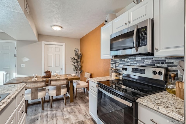 kitchen featuring white cabinetry, light hardwood / wood-style flooring, stainless steel appliances, light stone countertops, and backsplash