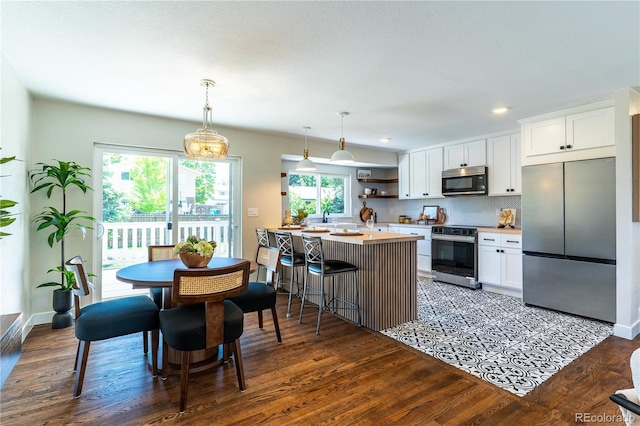 9410 Perry St, Westminster, CO 80031 - kitchen with appliances with stainless steel finishes, light countertops, dark wood finished floors, a breakfast bar area, and white cabinets