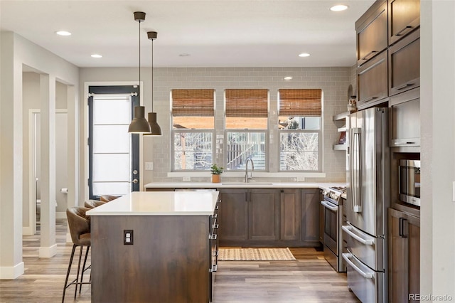 kitchen featuring a breakfast bar, pendant lighting, sink, light hardwood / wood-style floors, and stainless steel appliances