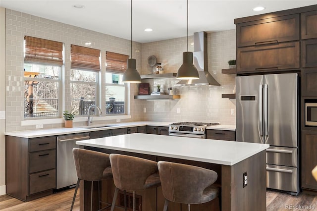 kitchen featuring a breakfast bar, sink, a center island, stainless steel appliances, and wall chimney exhaust hood