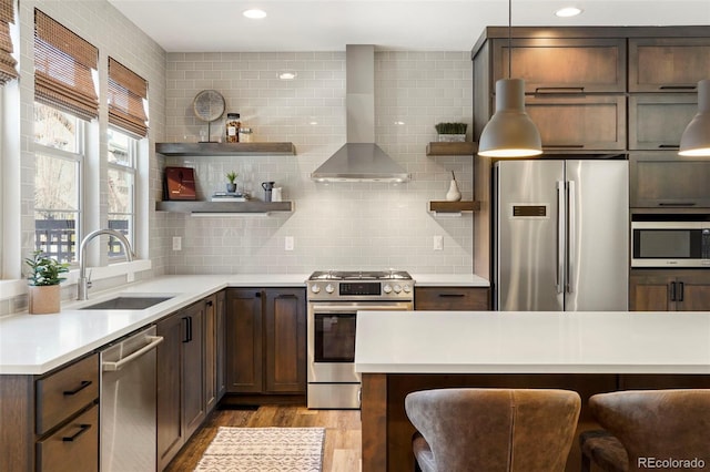 kitchen with stainless steel appliances, sink, a kitchen breakfast bar, and wall chimney exhaust hood