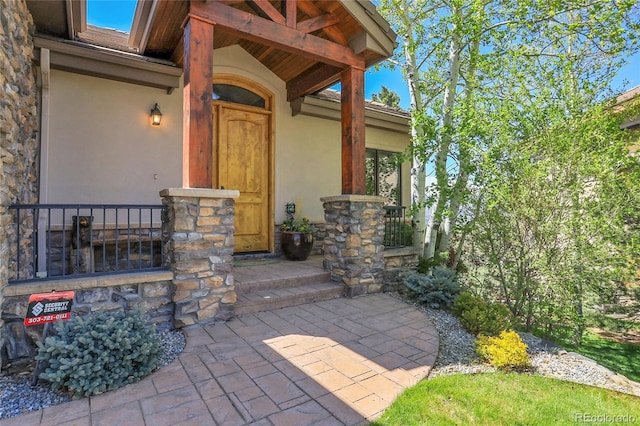 1007 Nob Hill Rd, Evergreen, CO 80439 - doorway to property with stucco siding, stone siding, and covered porch