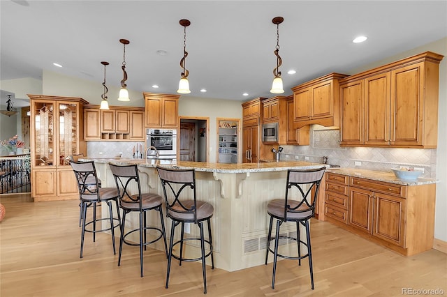 1007 Nob Hill Rd, Evergreen, CO 80439 - kitchen featuring light wood-style flooring, decorative backsplash, appliances with stainless steel finishes, a kitchen breakfast bar, and recessed lighting