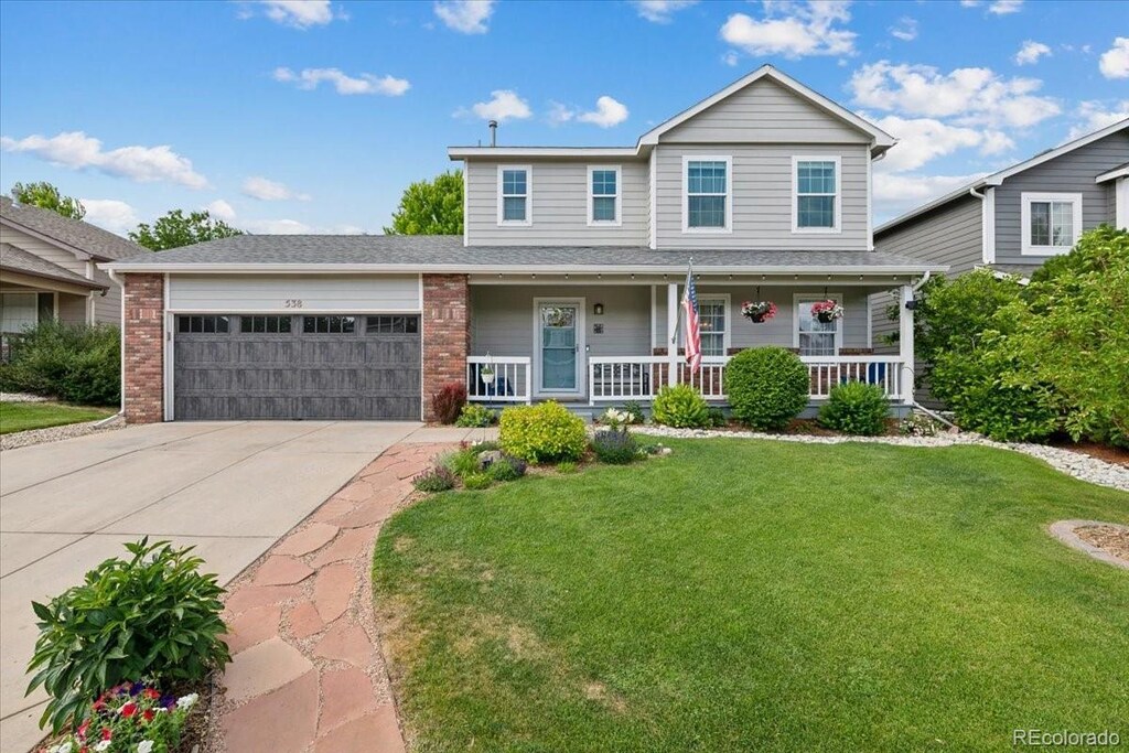 traditional home with covered porch, a front yard, driveway, and an attached garage