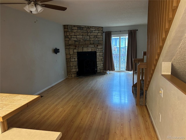 living room with ceiling fan, a stone fireplace, light hardwood / wood-style floors, and a textured ceiling