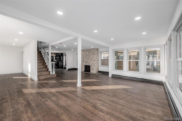 unfurnished living room featuring baseboard heating, a stone fireplace, and dark hardwood / wood-style floors