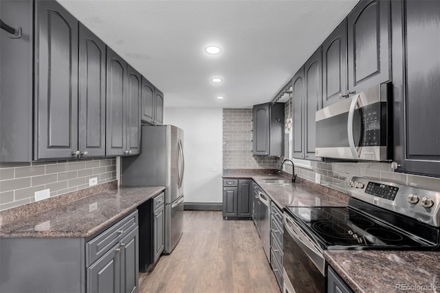 kitchen with appliances with stainless steel finishes, tasteful backsplash, dark stone counters, sink, and light hardwood / wood-style floors