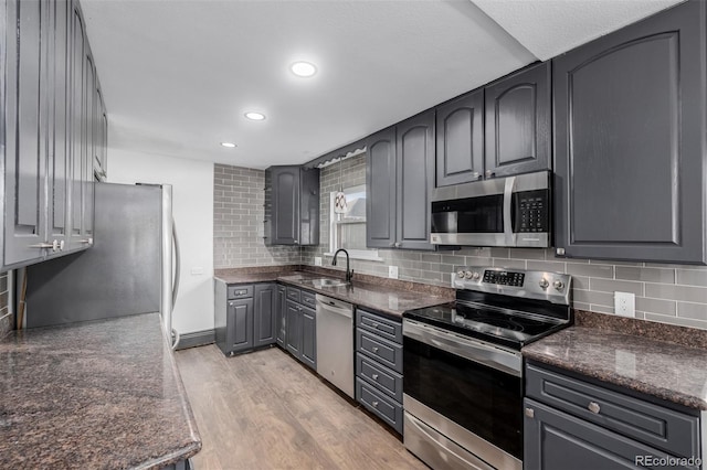 kitchen featuring gray cabinetry, sink, stainless steel appliances, tasteful backsplash, and light hardwood / wood-style flooring