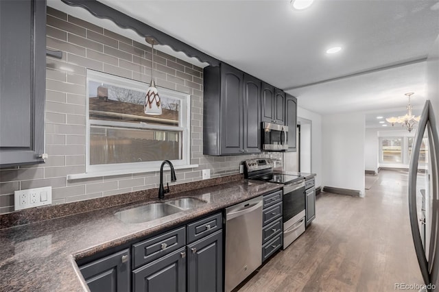 kitchen featuring sink, stainless steel appliances, backsplash, wood-type flooring, and decorative light fixtures