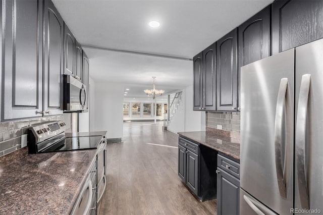 kitchen featuring dark stone counters, an inviting chandelier, appliances with stainless steel finishes, tasteful backsplash, and dark hardwood / wood-style flooring