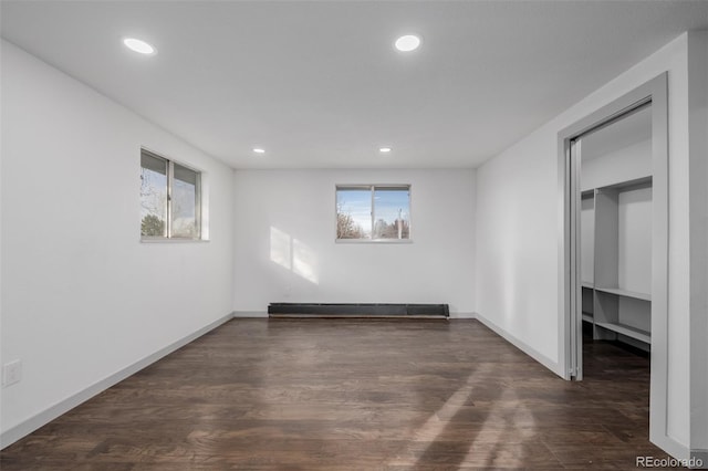 empty room featuring a healthy amount of sunlight, baseboard heating, and dark wood-type flooring