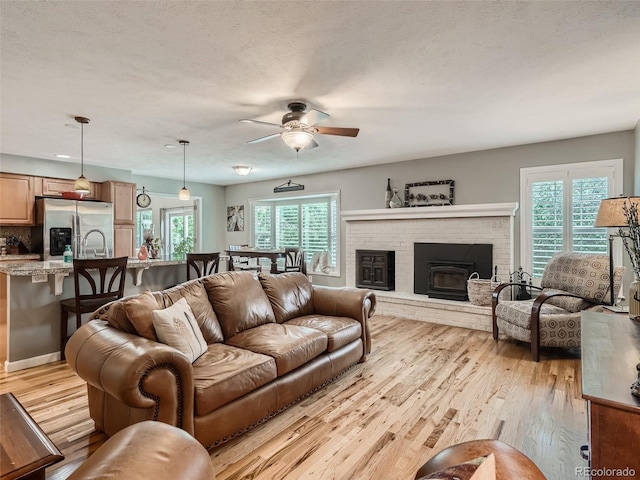 3265 W 11th Avenue Ct, Broomfield, CO 80020 - living area with a ceiling fan, light wood-type flooring, a brick fireplace, and a textured ceiling