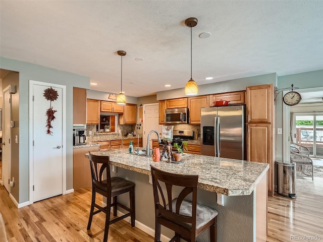 3265 W 11th Avenue Ct, Broomfield, CO 80020 - kitchen with stainless steel appliances, light wood-style floors, a sink, tasteful backsplash, and a kitchen bar