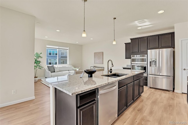 kitchen with light wood-style floors, light stone countertops, a kitchen island with sink, a sink, and stainless steel appliances
