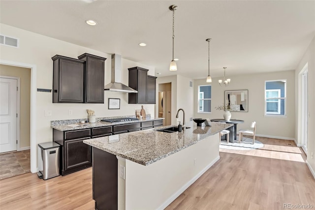 kitchen featuring visible vents, a sink, wall chimney range hood, stainless steel gas cooktop, and light stone counters