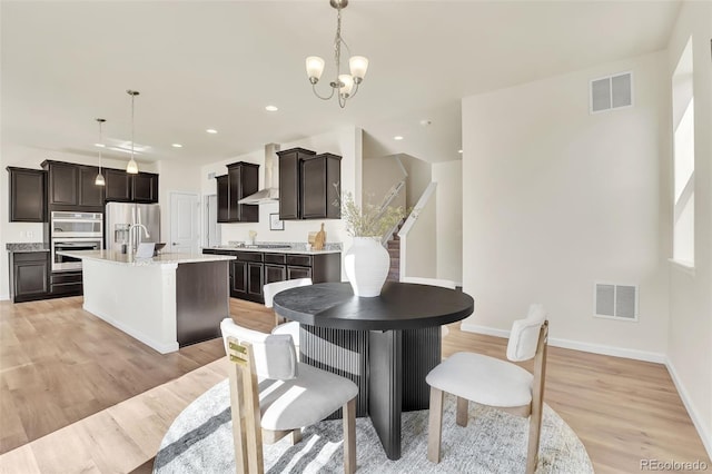 dining space featuring light wood finished floors, baseboards, visible vents, and a notable chandelier