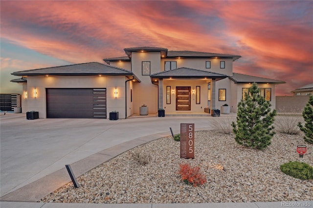 prairie-style house featuring stucco siding, a tile roof, an attached garage, and concrete driveway