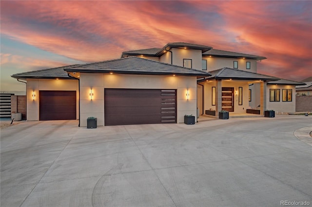 prairie-style house featuring concrete driveway, stucco siding, a tiled roof, and a garage