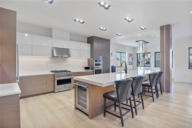 kitchen with beverage cooler, wall chimney exhaust hood, appliances with stainless steel finishes, and modern cabinets