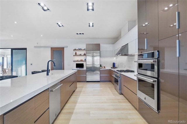 kitchen featuring light wood finished floors, a sink, modern cabinets, light countertops, and high quality appliances