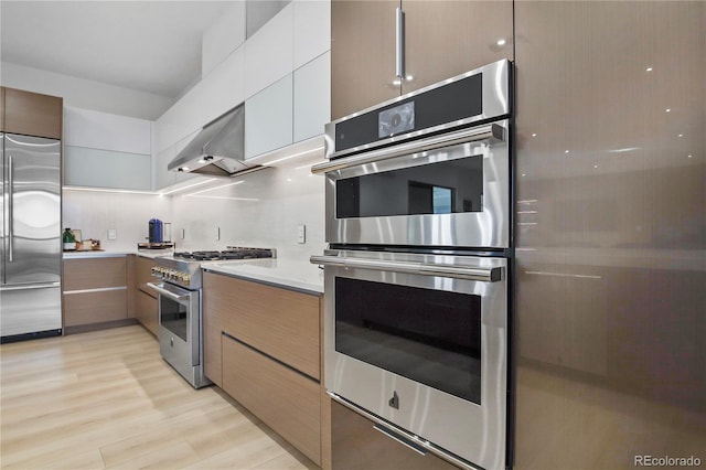 kitchen with modern cabinets, wall chimney range hood, high quality appliances, and light countertops