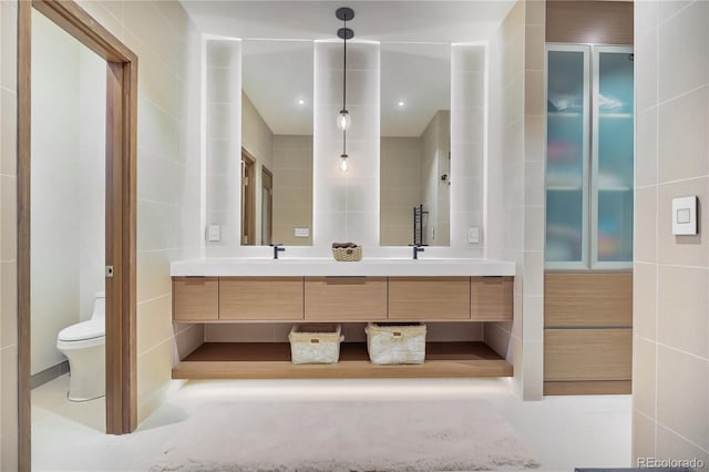 bathroom with double vanity, toilet, tile walls, and a sink