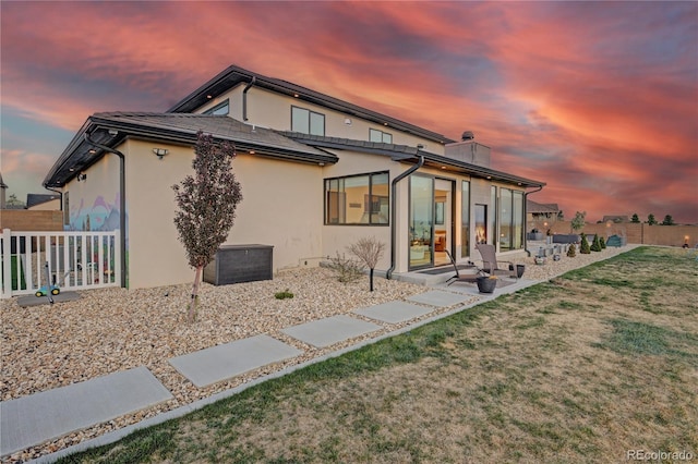 back of property featuring a chimney, fence, a yard, a patio, and stucco siding