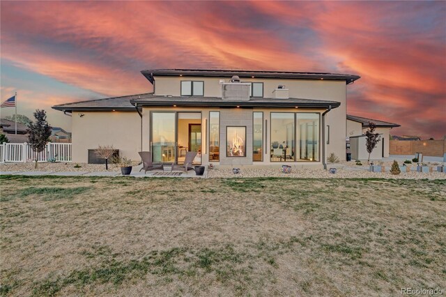 back of house at dusk with fence, a lawn, a patio area, and stucco siding