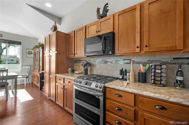 1210 Muskox St, Severance, CO 80550 - kitchen featuring range with two ovens, black microwave, decorative backsplash, brown cabinetry, and vaulted ceiling