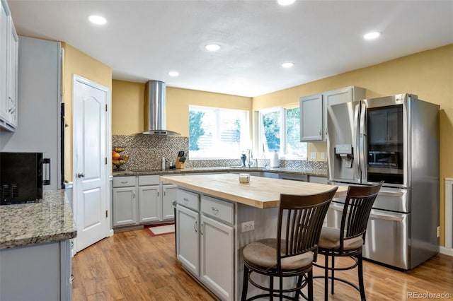 801 S 15th Ave, Brighton, CO 80601 - kitchen featuring stainless steel appliances, range hood, butcher block countertops, a kitchen bar, and light wood-style floors