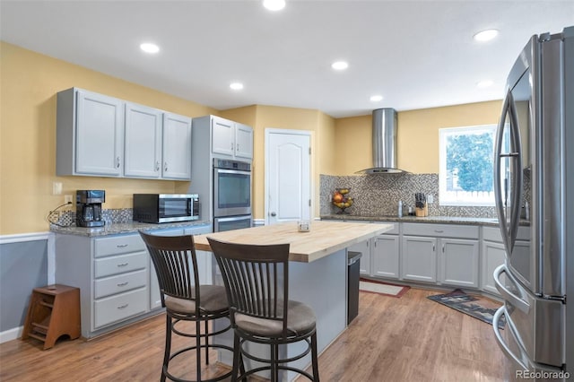 801 S 15th Ave, Brighton, CO 80601 - kitchen with stainless steel appliances, wall chimney exhaust hood, butcher block counters, a kitchen bar, and light wood-type flooring
