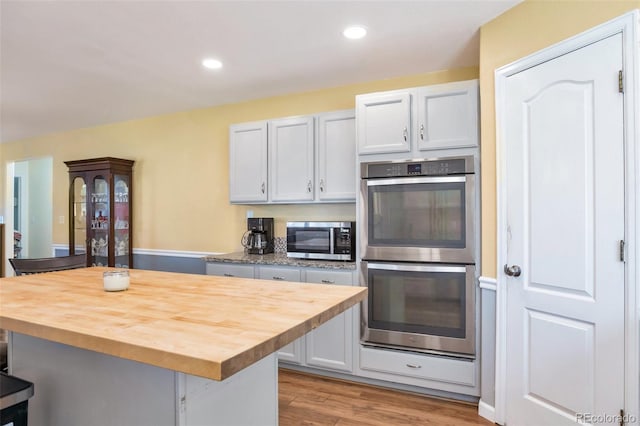 801 S 15th Ave, Brighton, CO 80601 - kitchen with appliances with stainless steel finishes, wood counters, a kitchen breakfast bar, light wood-style floors, and a center island