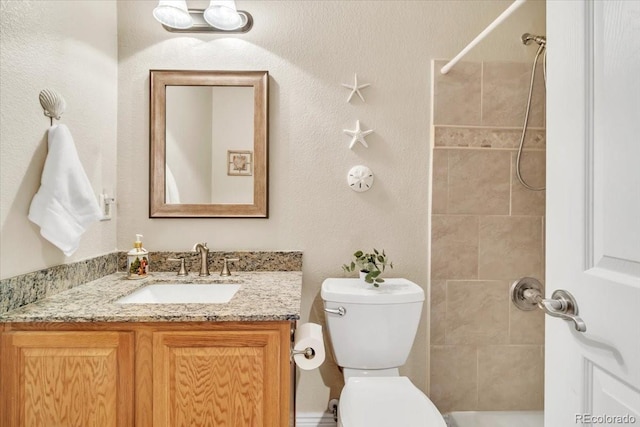 bathroom with toilet, vanity, and a tile shower